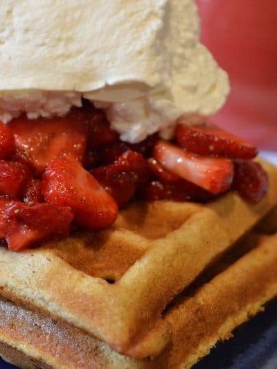 A plate with waffles, strawberries and whipped cream.