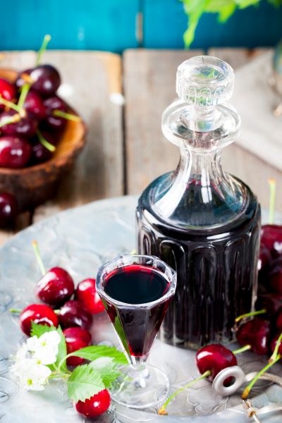 Cherry liqueur in a decanter and glass beside fresh cherries