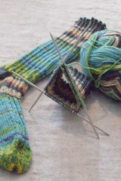 One completed knitted sock, a ball of yarn and a yarn on three needles.