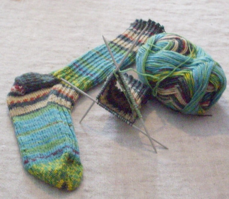 One completed knitted sock, a ball of yarn and a yarn on three needles.