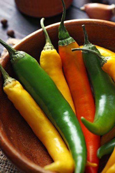 A wooden bowl with orange, yellow and green hot peppers