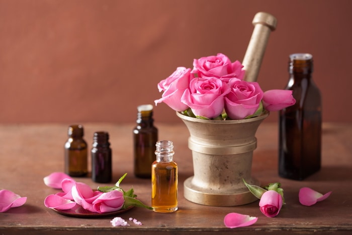 Pink roses in a mortar and pestle. Rose petals scattered around and apothecary bottles on a table