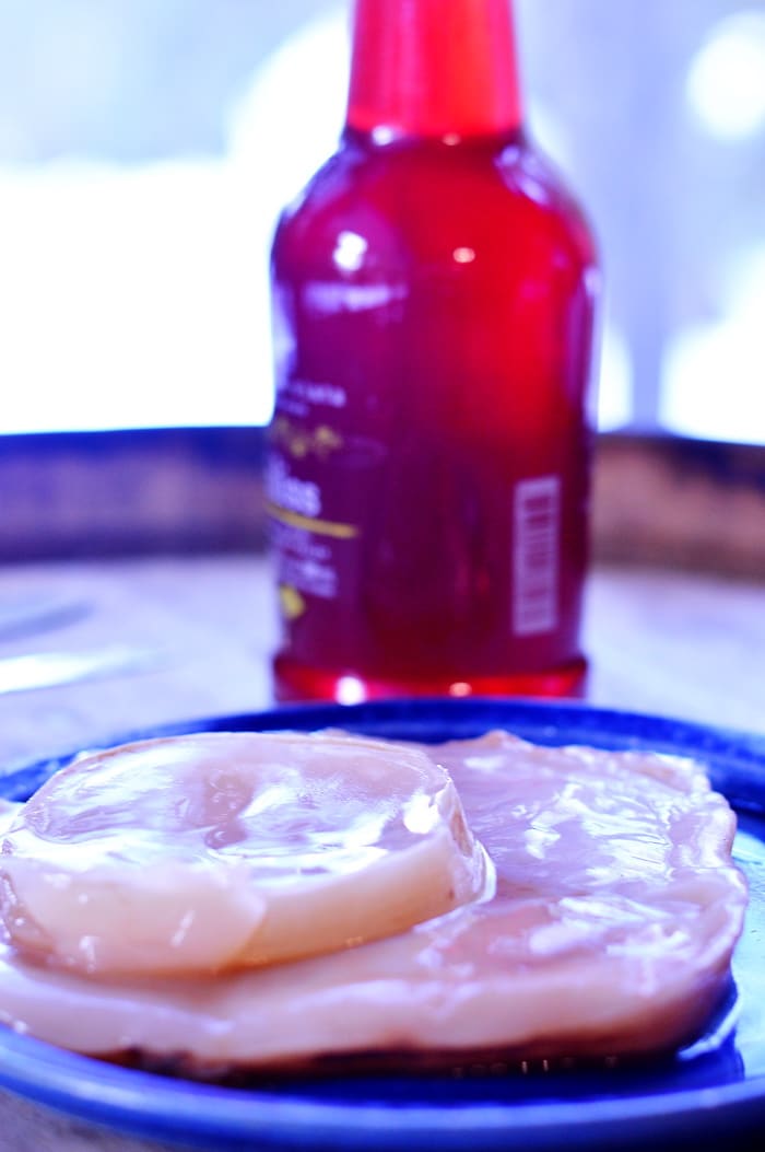 A plate with a couple of Kombucha scoby on it in front of a glass bottle filled with Kombucha