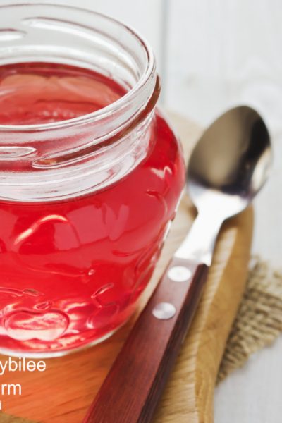 clear red pepper jelly in a glass jar alongside a serving spoon