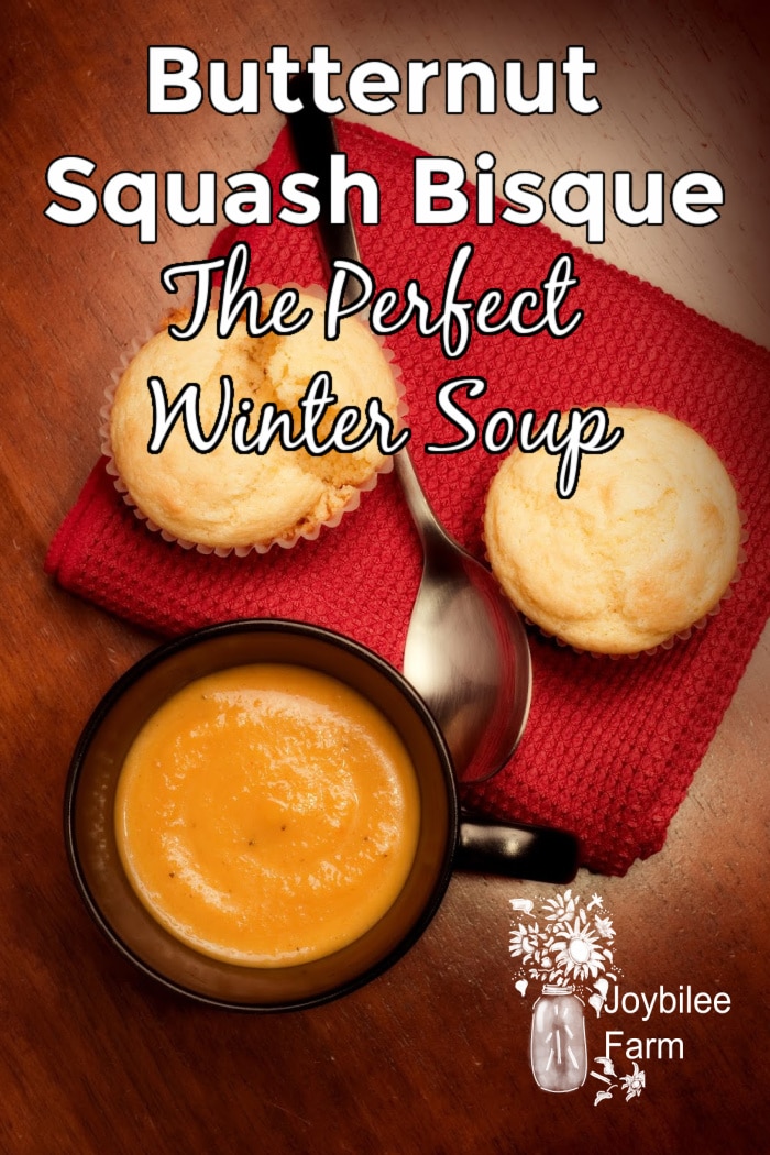 A mug full of creamy butternut squash bisque with corn muffins on a wooden table.