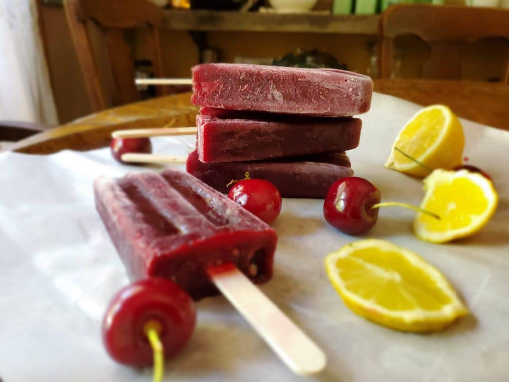 cherry lemonade popsicle with fresh cherries and lemon slices on a wooden board