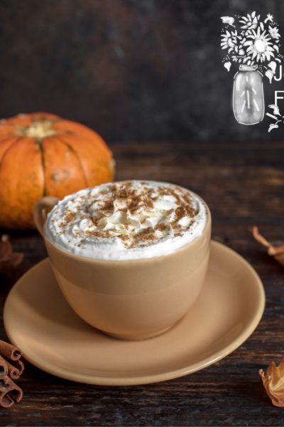 A pumpkin spice latte on a dark wooden table with a pumpkin in the background