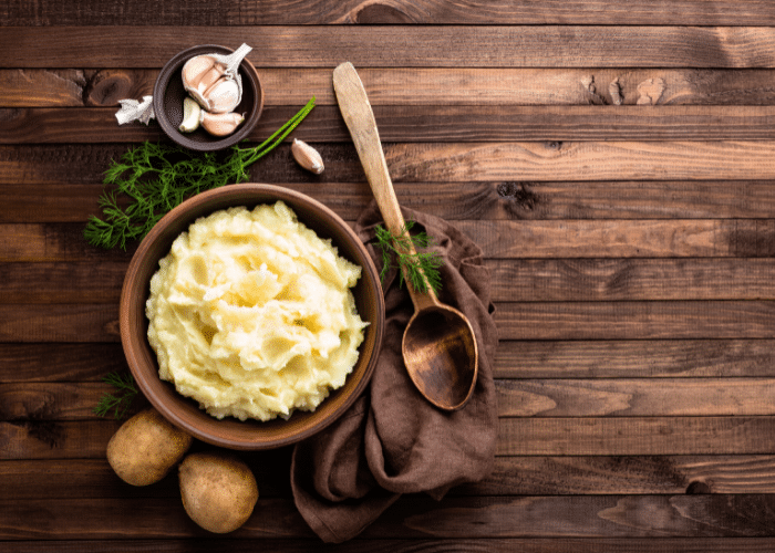 mashed potatoes on a brown wooden background with garlic, dill, and whole potatoes around them