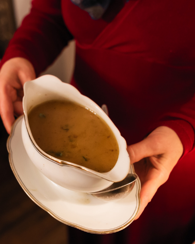 gravy in a white gravy boat being brought to the table by a womean in a red top