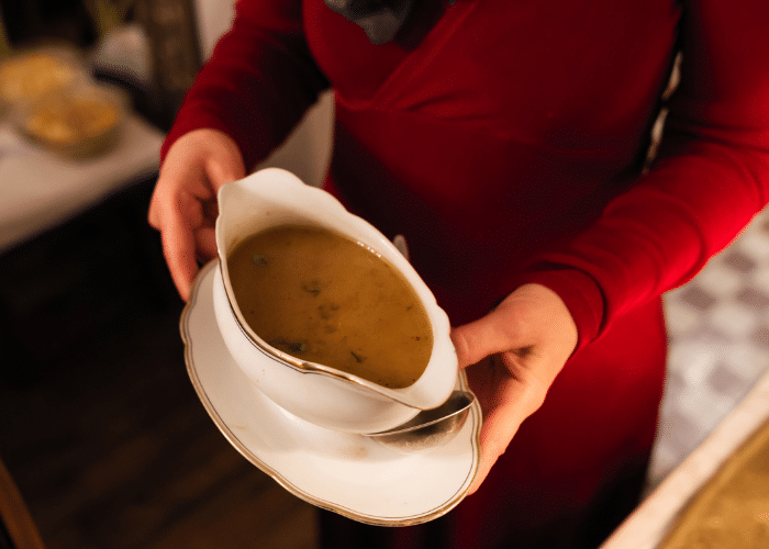 gravy in a white gravy boat being brought to the table by a womean in a red top