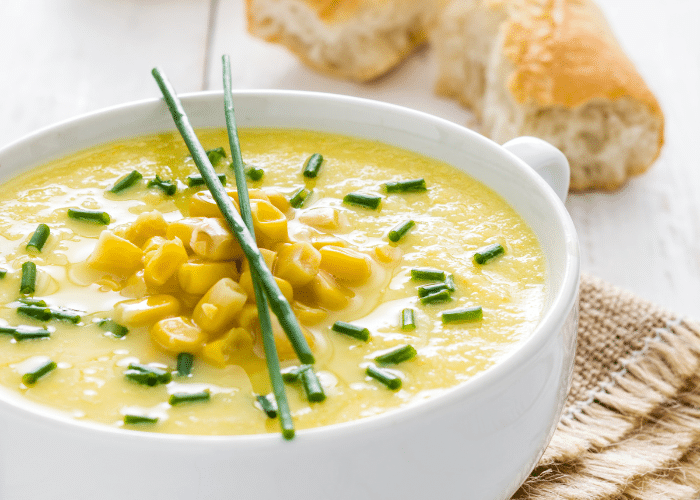 cream of corn soup in a white bowl with whole corn kernels on top and green onions or chives sprinkled around.