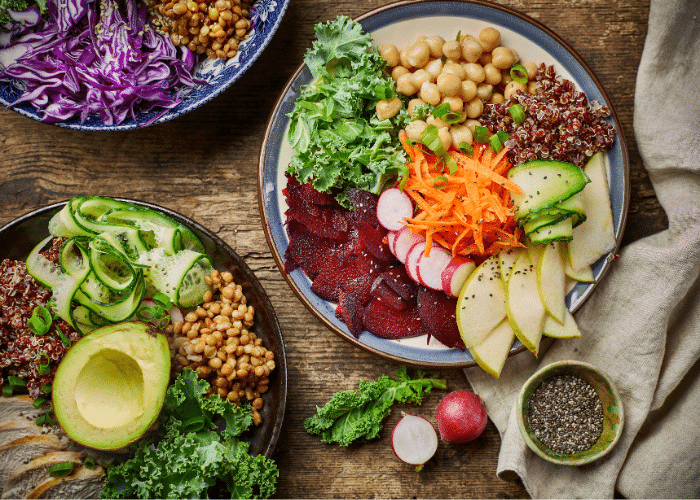 a collection of 3 healthy bowls with chickpeas, avocado, shredded carrots and red cabbage, kale, and other vegetables visible on the surface of the rice bowl.